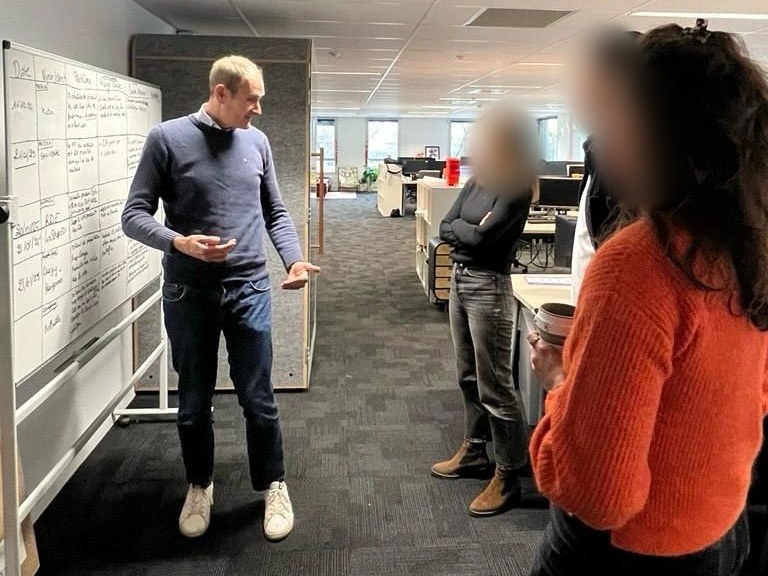 Charles Bourinet échange avec une équipe devant un tableau de suivi, dans des bureaux